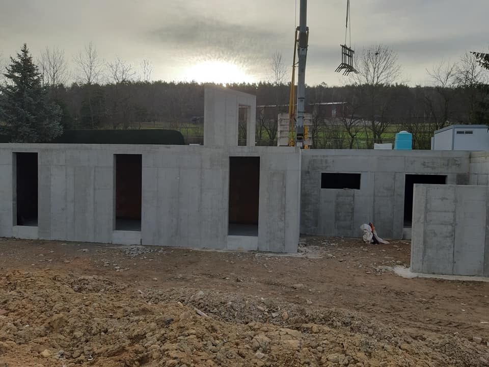 Structure en béton en construction à l'extérieur ; portes ouvertes, grue en arrière-plan, ciel couvert.