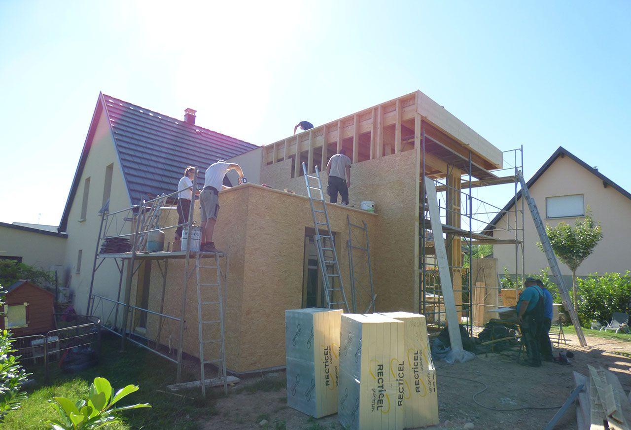Des ouvriers du bâtiment construisent une extension de maison avec une charpente et des lambris en bois par une journée ensoleillée.