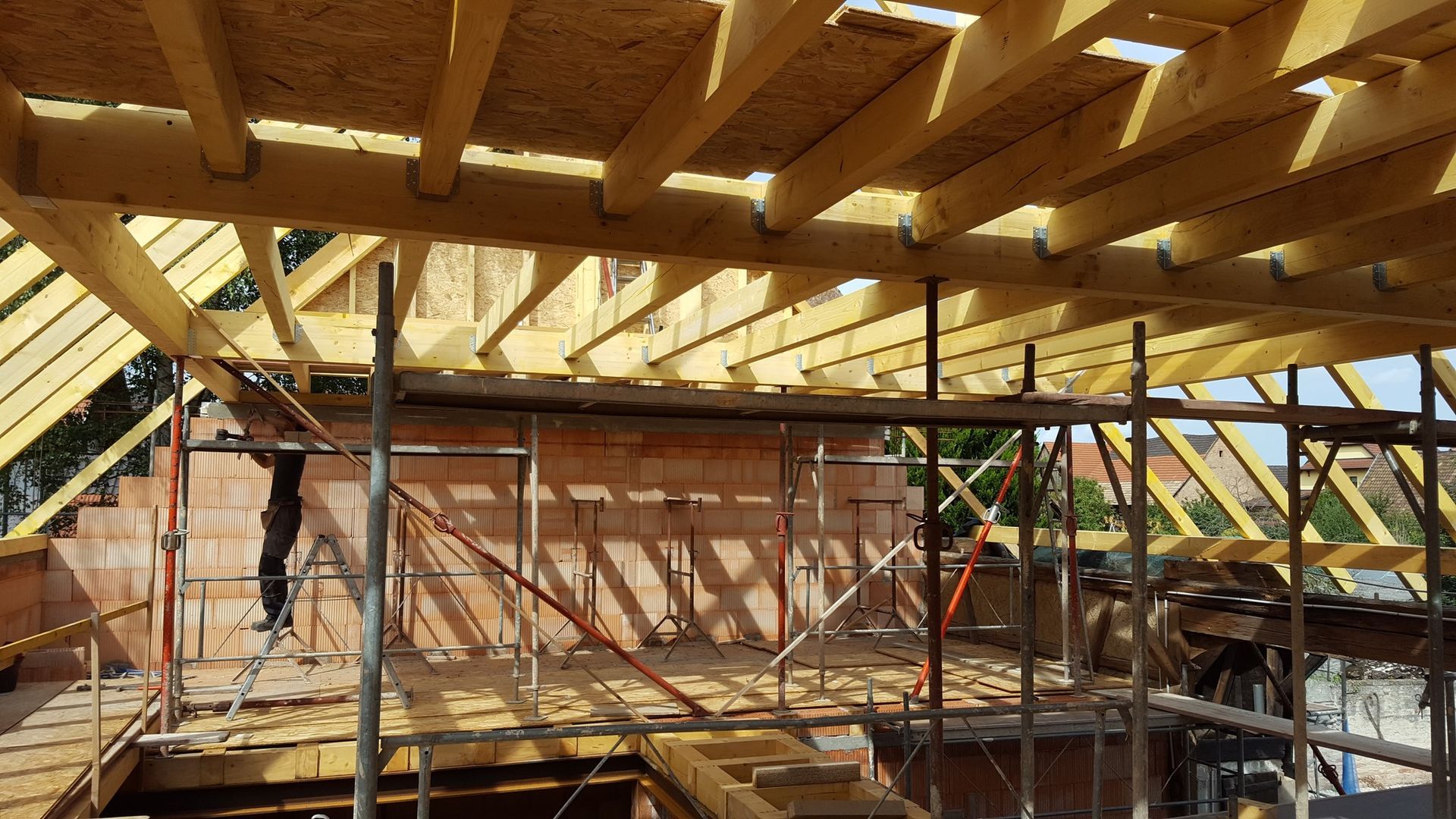 Chantier de construction avec poutres apparentes, échafaudages et murs de briques.