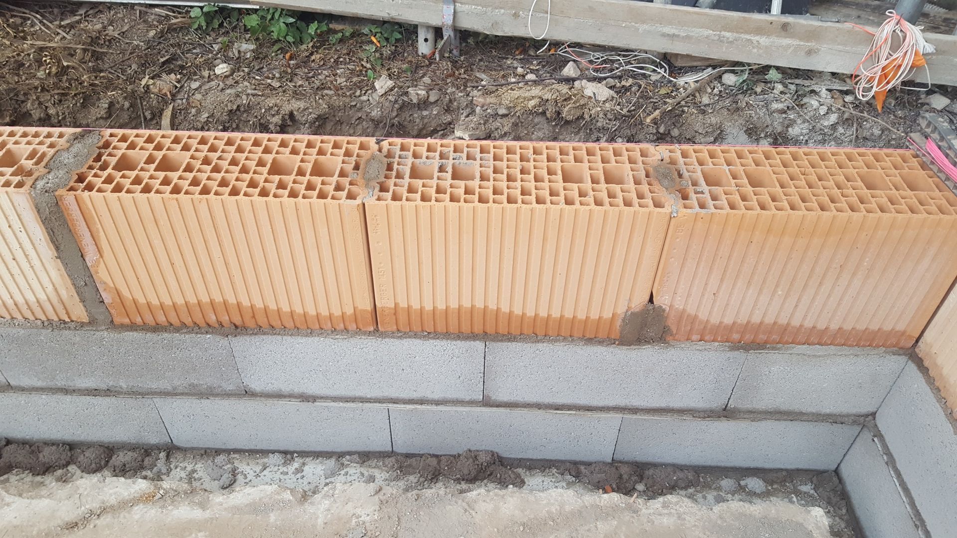 Mur de briques rouges en construction sur des blocs de béton gris.