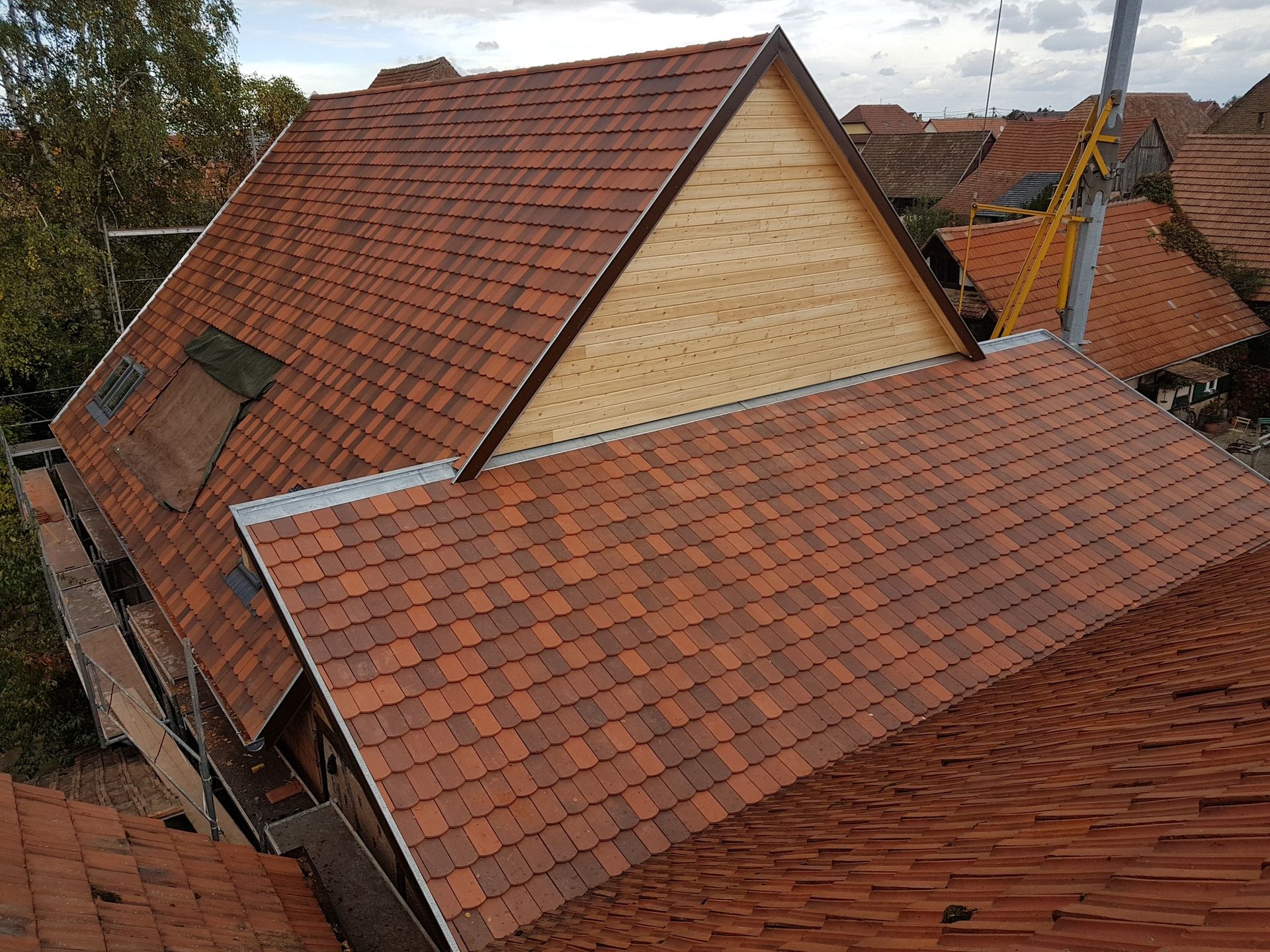 Toit de tuiles rouges d'un bâtiment en construction, avec un pignon en bois clair.
