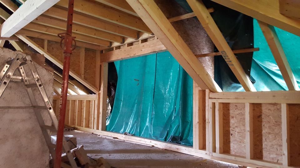 Vue intérieure d'un bâtiment en construction, à ossature de poutres en bois, avec une bâche recouvrant l'ouverture et une poutre de soutien.