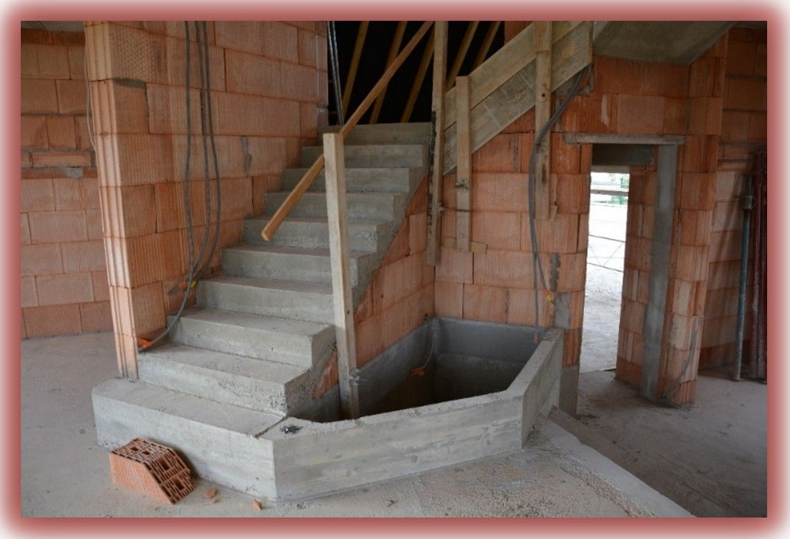 Vue intérieure d'un bâtiment en construction, montrant un escalier en béton, des murs et une porte.