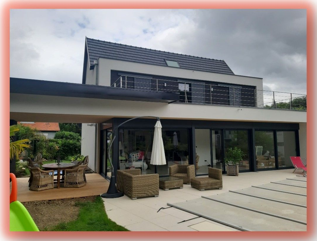 Maison moderne avec terrasse, piscine et mobilier de jardin sous un ciel nuageux.