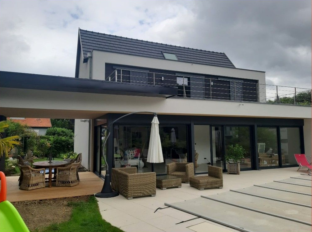 Extérieur d'une maison moderne avec coin salon extérieur, terrasse et piscine sous un ciel nuageux.