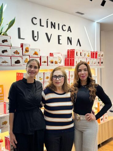 Tres mujeres posan frente al letrero y la exhibición de productos de una clínica.