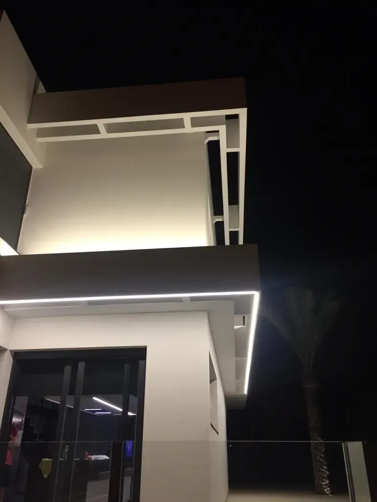 Exterior de una casa moderna por la noche con molduras blancas brillantes y ventanas oscuras contra un cielo negro.