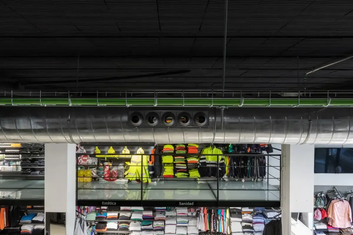 Techo de la tienda con conductos de ventilación a la vista y estantes con mercancía colorida en la parte inferior.