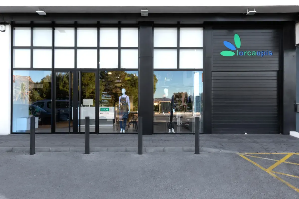 Entrada moderna a la tienda con puertas de cristal, bolardos negros y un letrero en el lado derecho.