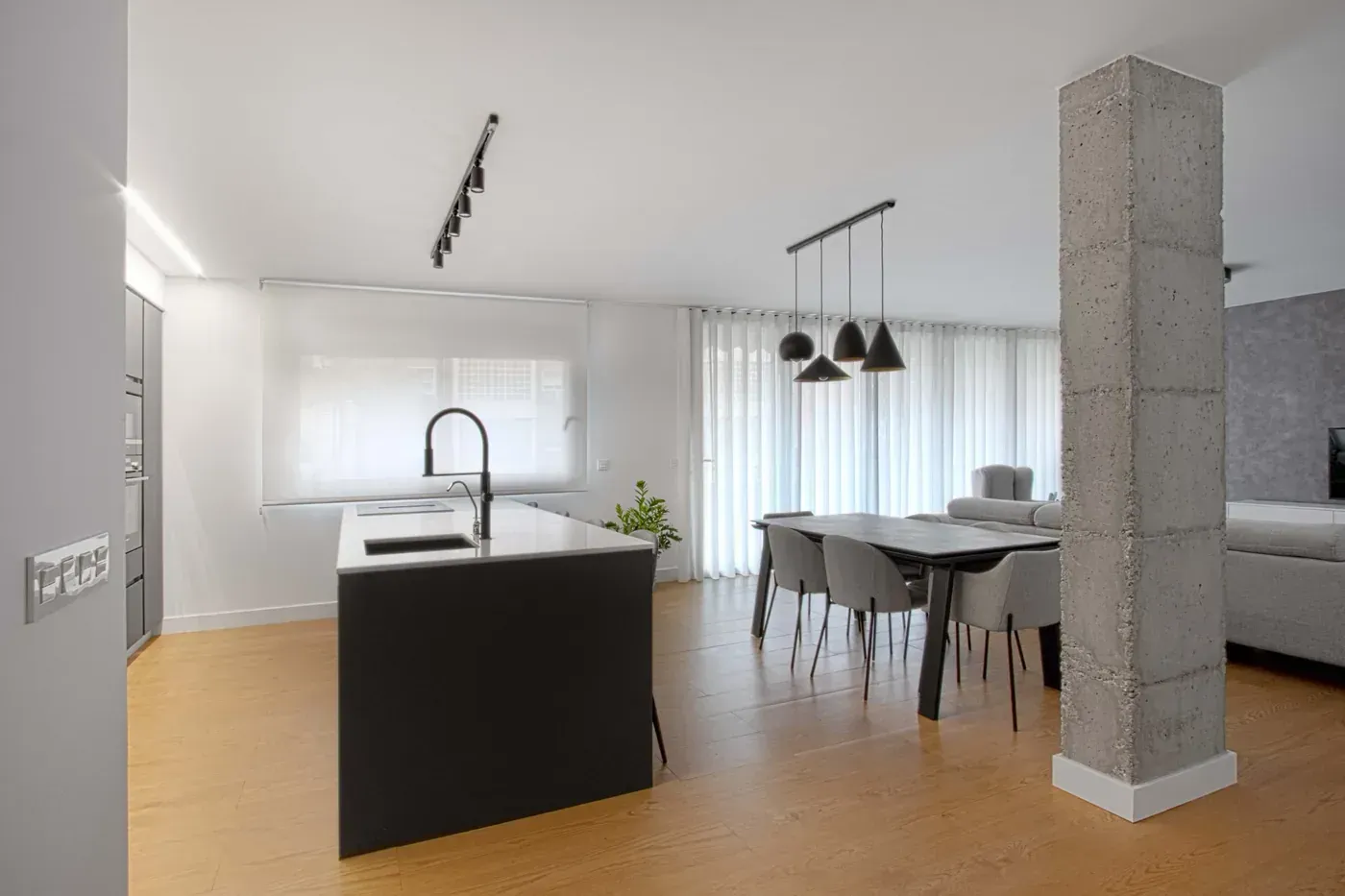 Cocina y comedor modernos de planta abierta con isla, sillas negras, lámparas colgantes y grandes ventanales.