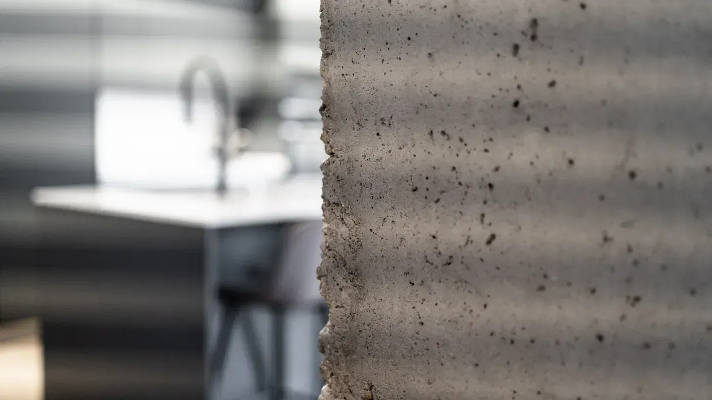 Primer plano de una pared de hormigón gris con un interior moderno difuminado al fondo.