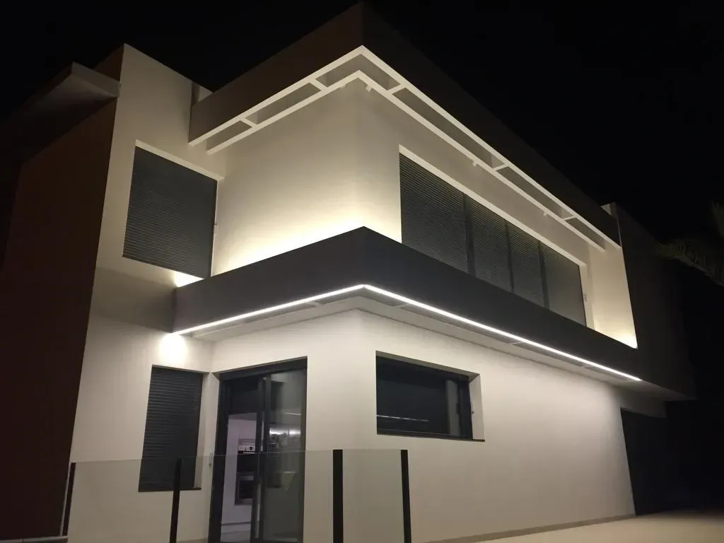 Casa moderna blanca de dos plantas por la noche, iluminada por luces exteriores y vista desde abajo.