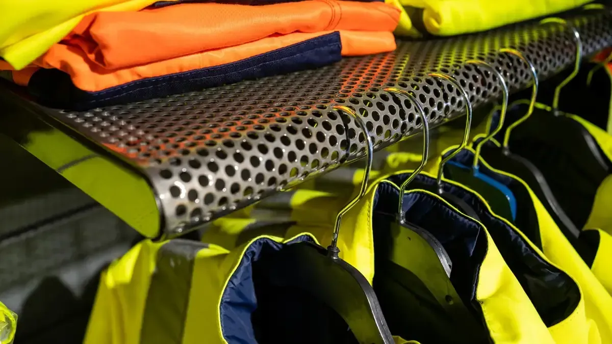 Chalecos salvavidas de color amarillo neón y negro apilados en un estante, con equipo de seguridad naranja doblado encima.