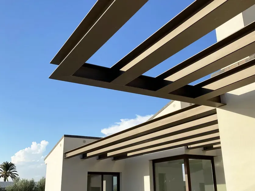 Patio de casa moderna con pérgola de vigas oscuras bajo un cielo azul