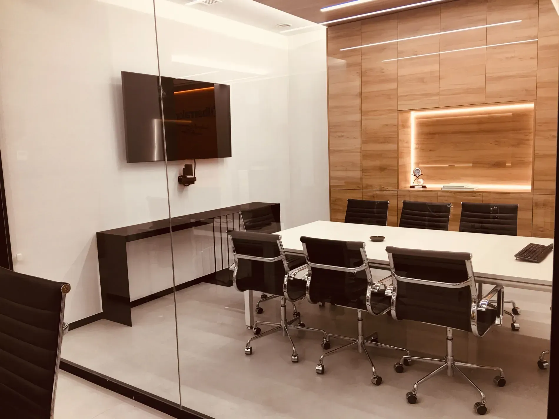 Moderna sala de conferencias con mesa de cristal, sillas negras, televisor montado en la pared