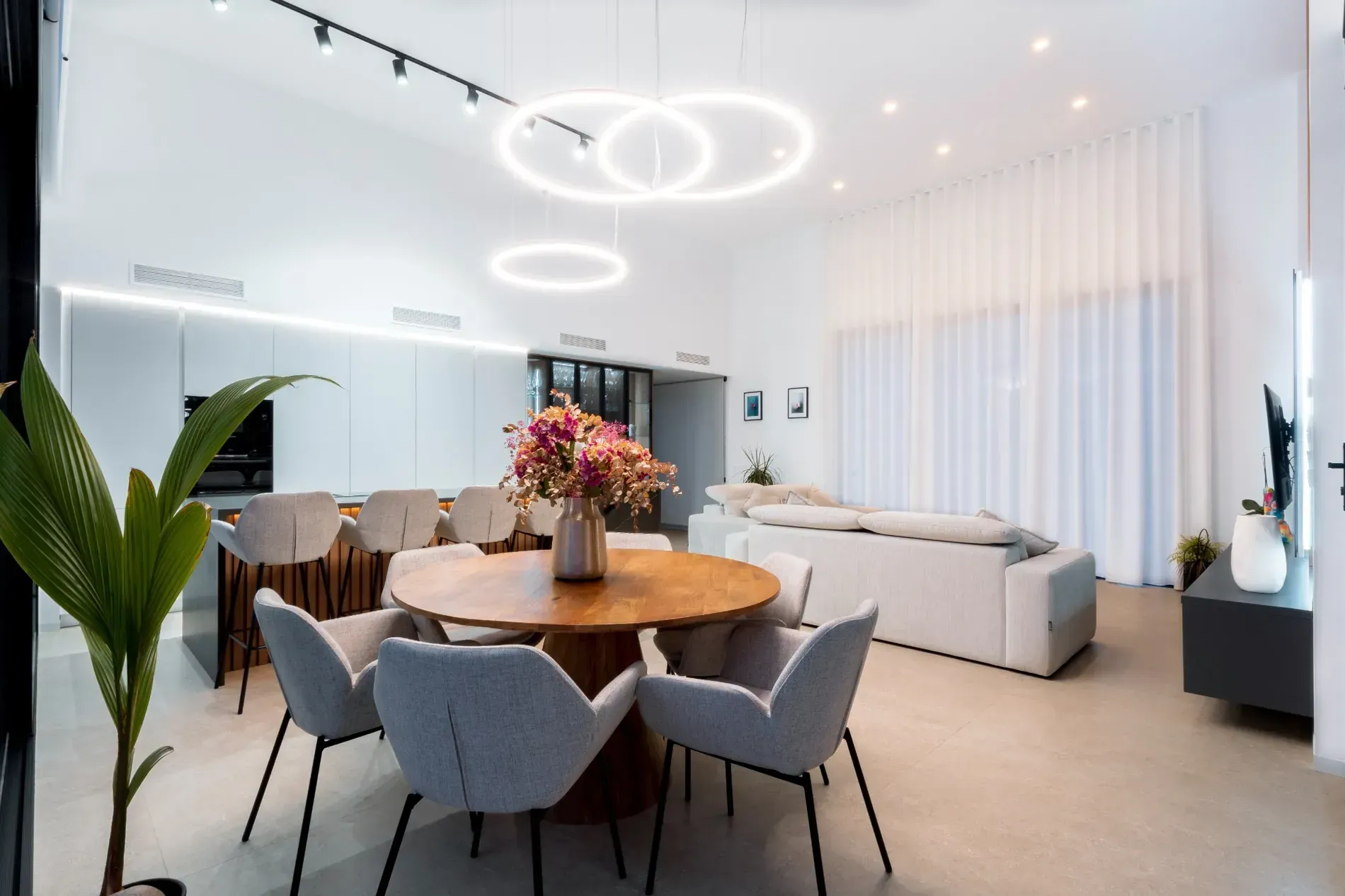 Salón moderno de planta abierta con mesa de comedor, sofás grises y lámparas de techo circulares.