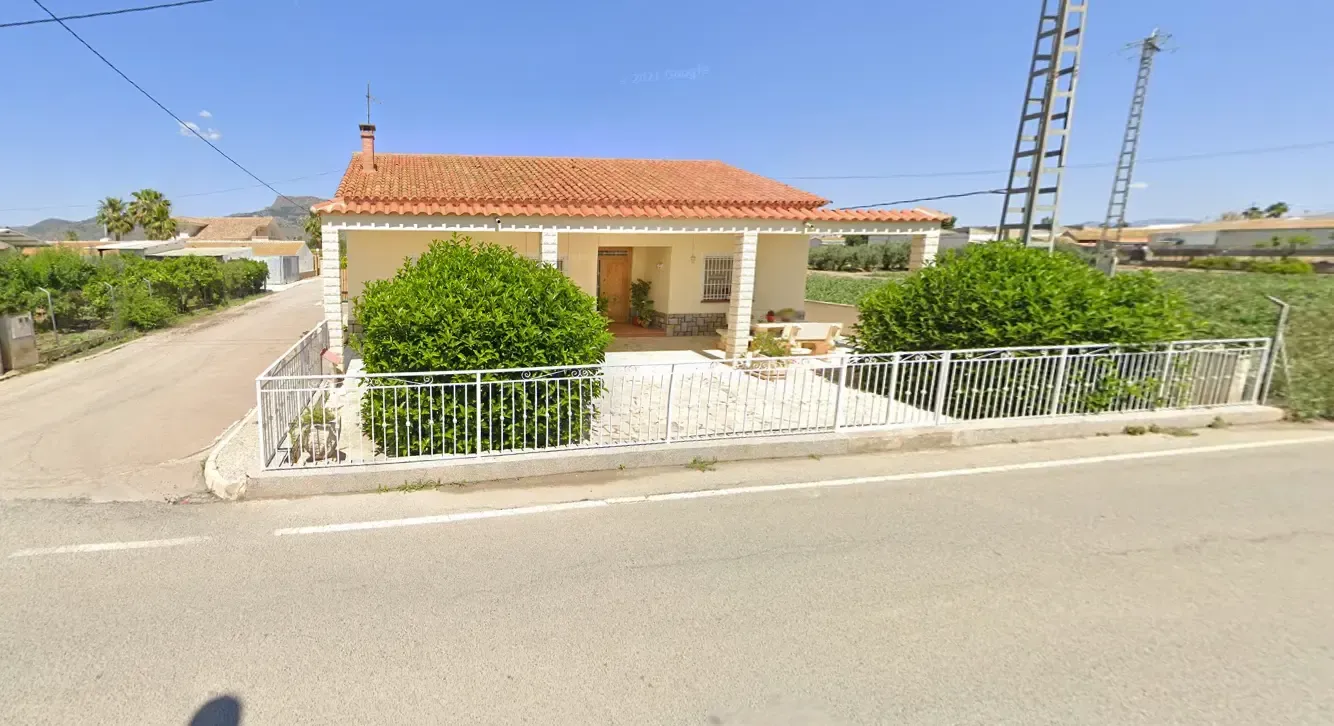 Casa de una sola planta de color crema con techo de tejas rojas y valla blanca