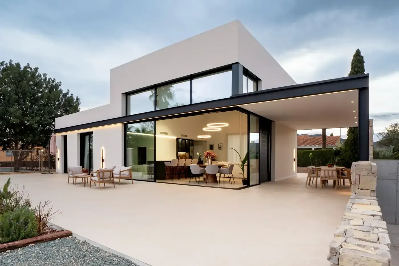 Moderna casa de vidrio y hormigón con terraza abierta para sentarse al atardecer.