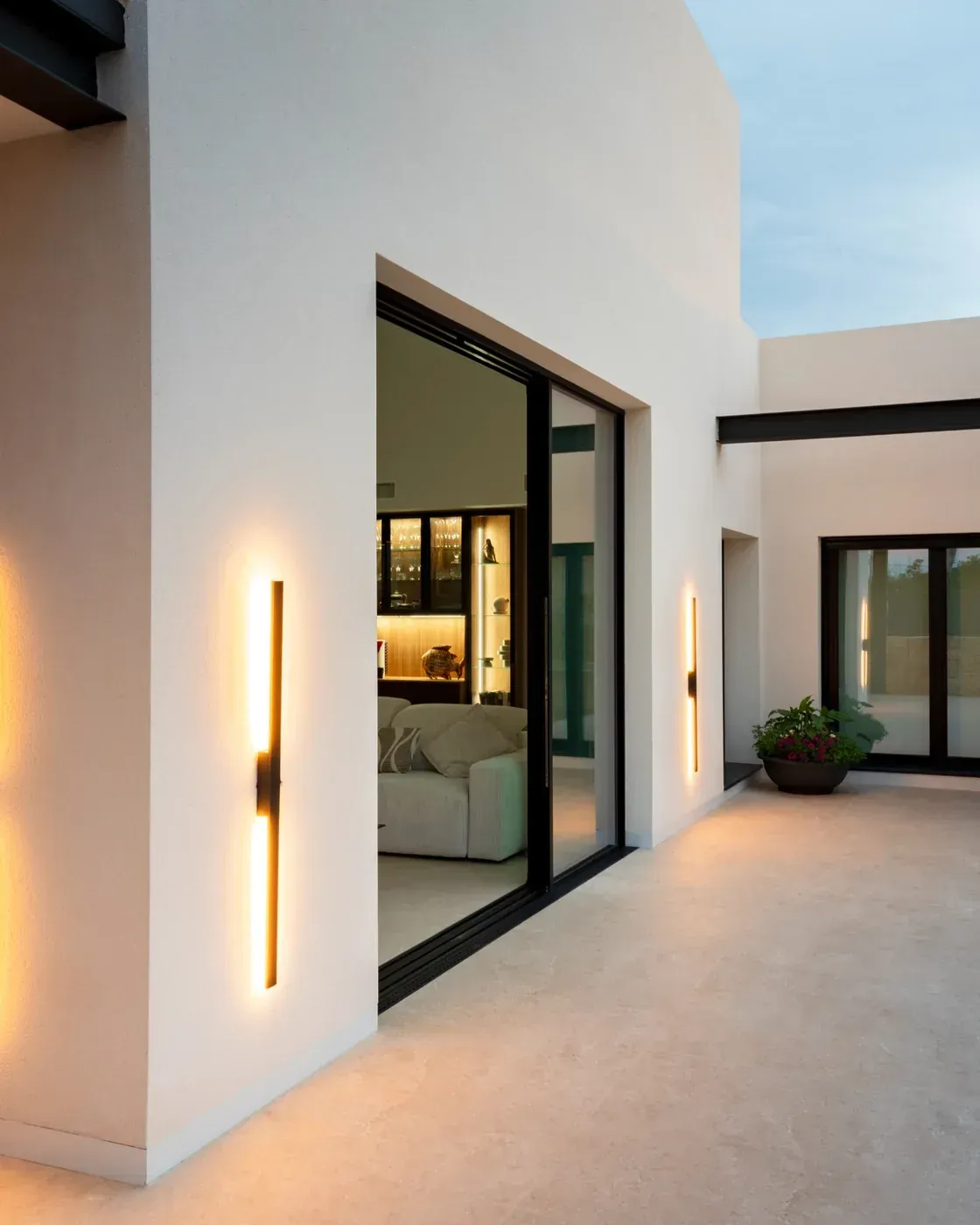 Patio moderno blanco con puertas corredizas de vidrio y apliques de pared cálidos.