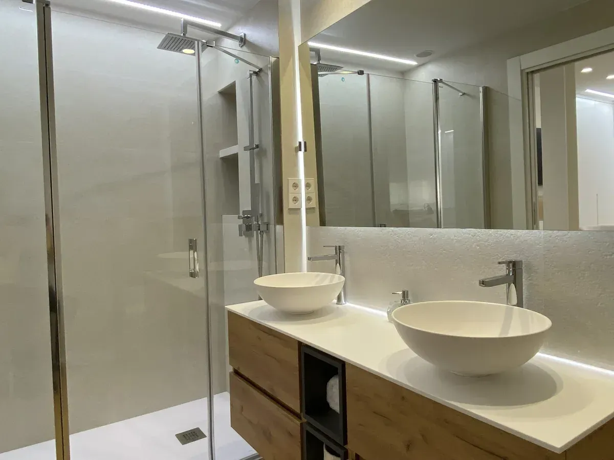 Baño moderno con ducha de cristal, lavabos dobles y espejos grandes.