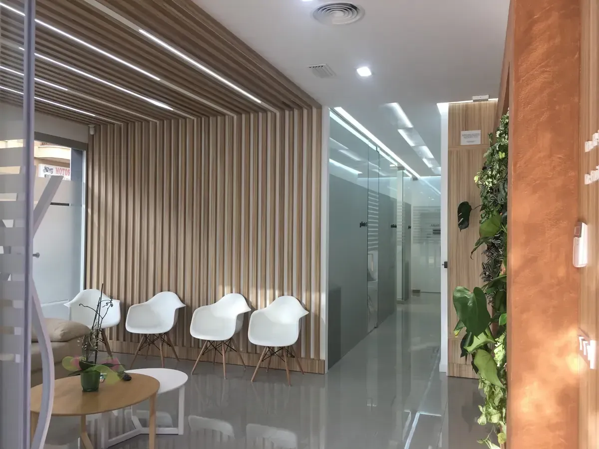Vestíbulo de oficina moderno con sillas blancas, techo de listones de madera, paredes de vidrio y plantas de interior.