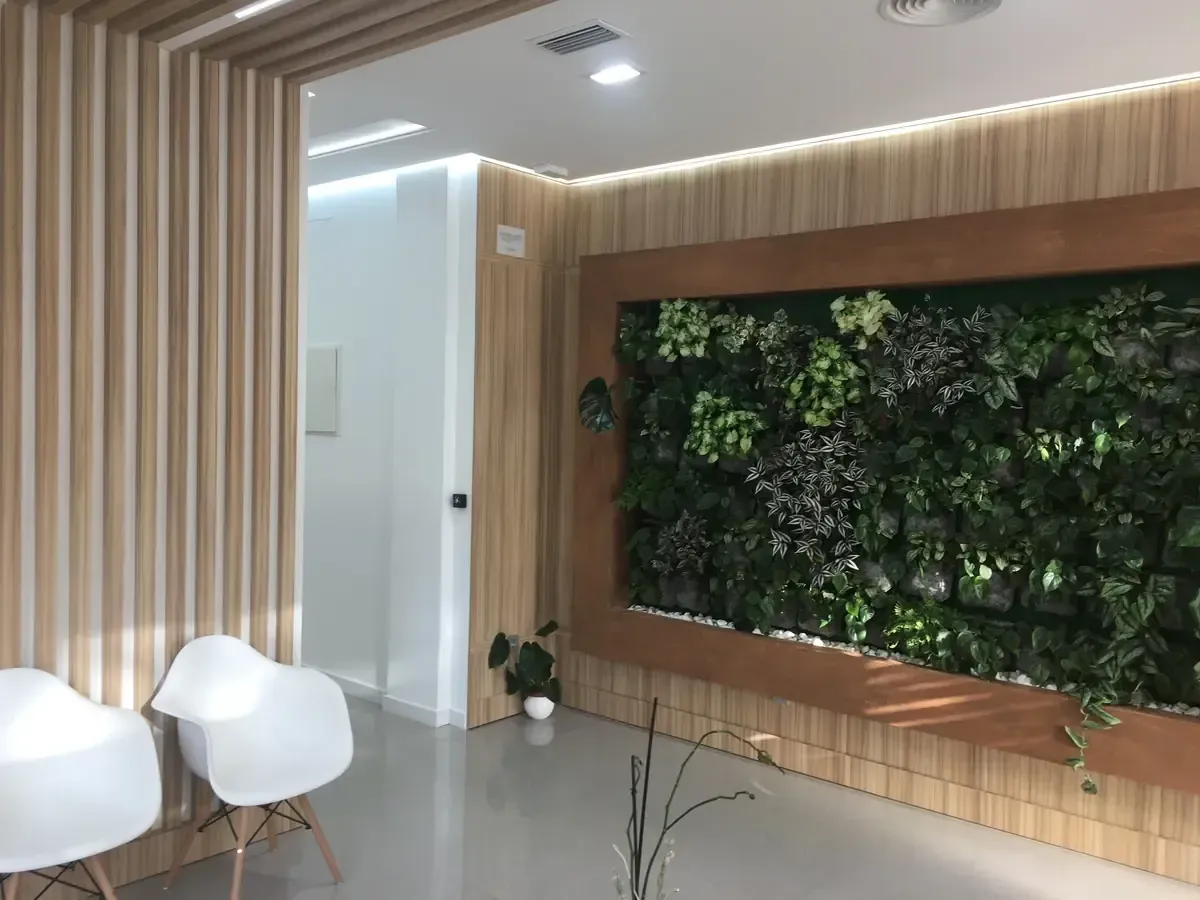 Interior moderno con sillas blancas, paredes revestidas de listones de madera y una pared con plantas verdes.