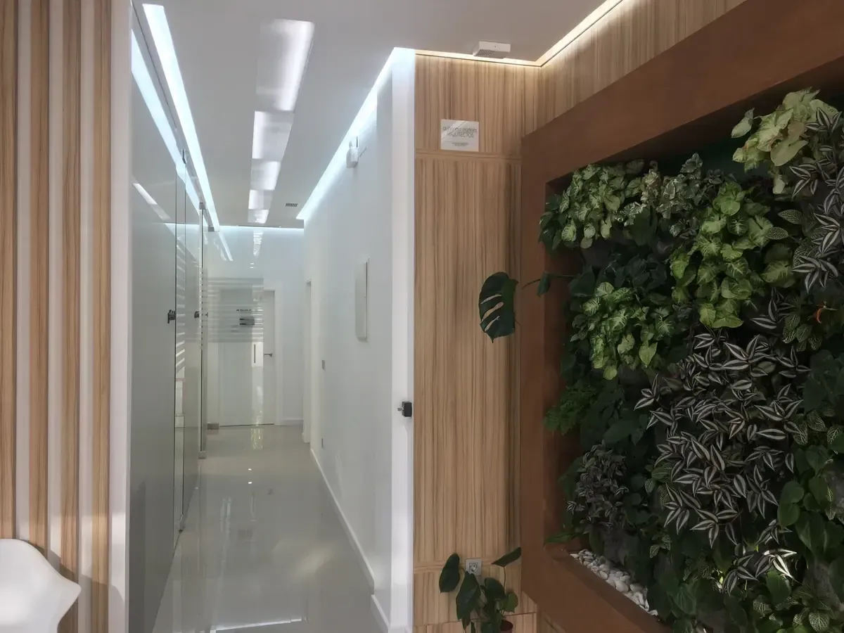 Pasillo moderno con paredes revestidas de listones de madera, suelo blanco y una pared vegetal verde a la derecha.