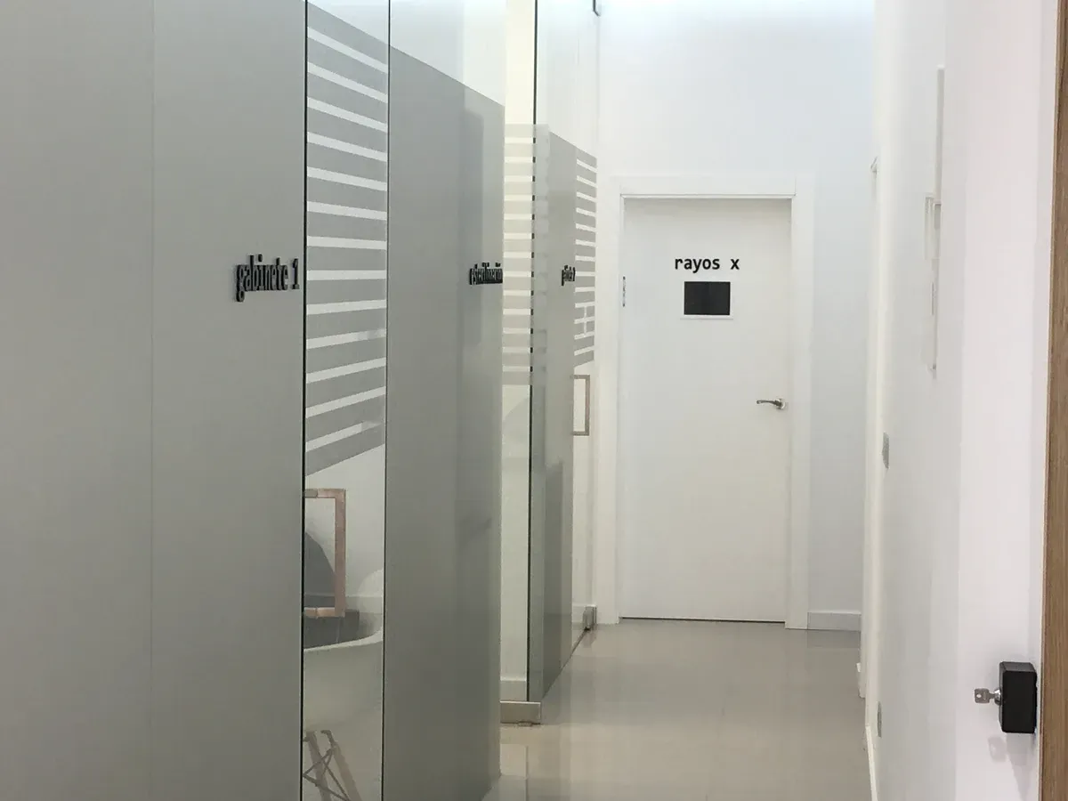 Pasillo blanco luminoso con mamparas de cristal para oficinas y una puerta al final.
