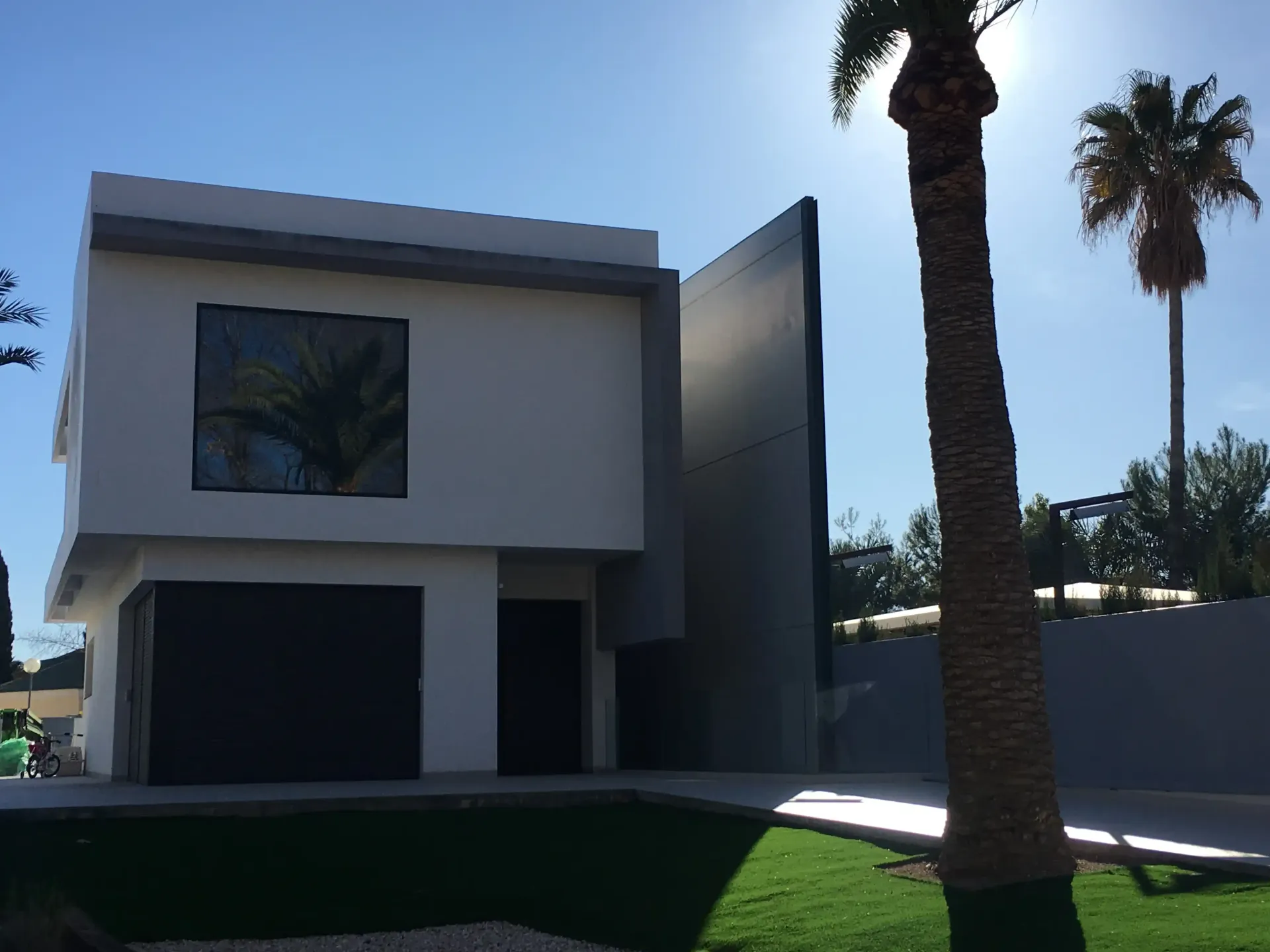 Casa moderna de dos plantas con una palmera y cielo azul en primer plano.