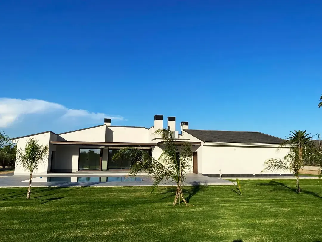 Casa blanca moderna con piscina y palmeras bajo un cielo azul despejado.