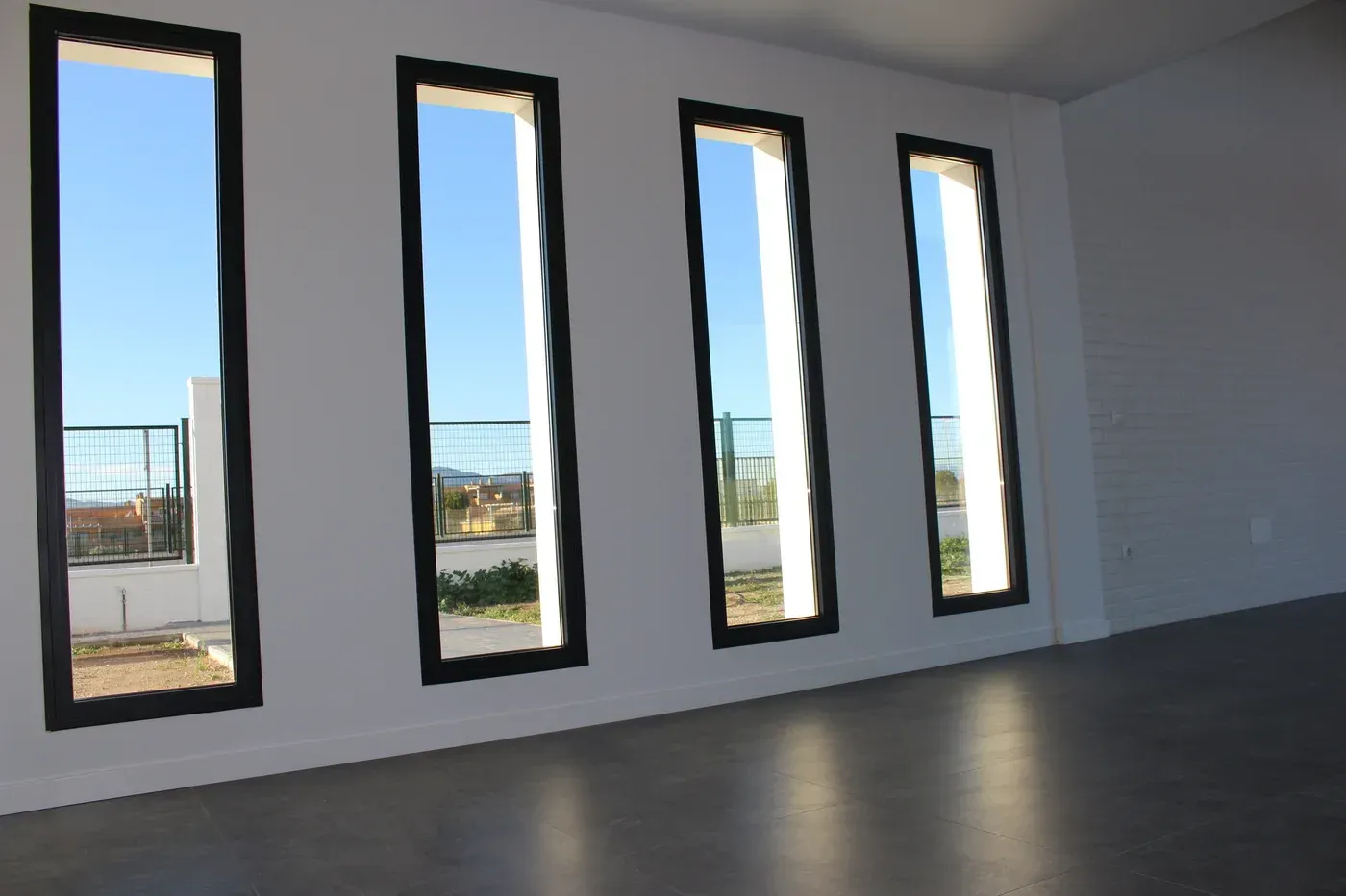Habitación moderna vacía con cuatro ventanas altas y estrechas y vistas al exterior.