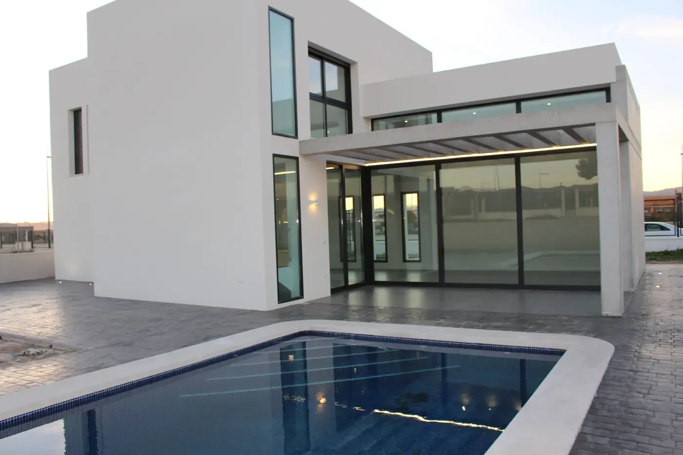 Casa blanca moderna con grandes ventanales y una piscina en primer plano.