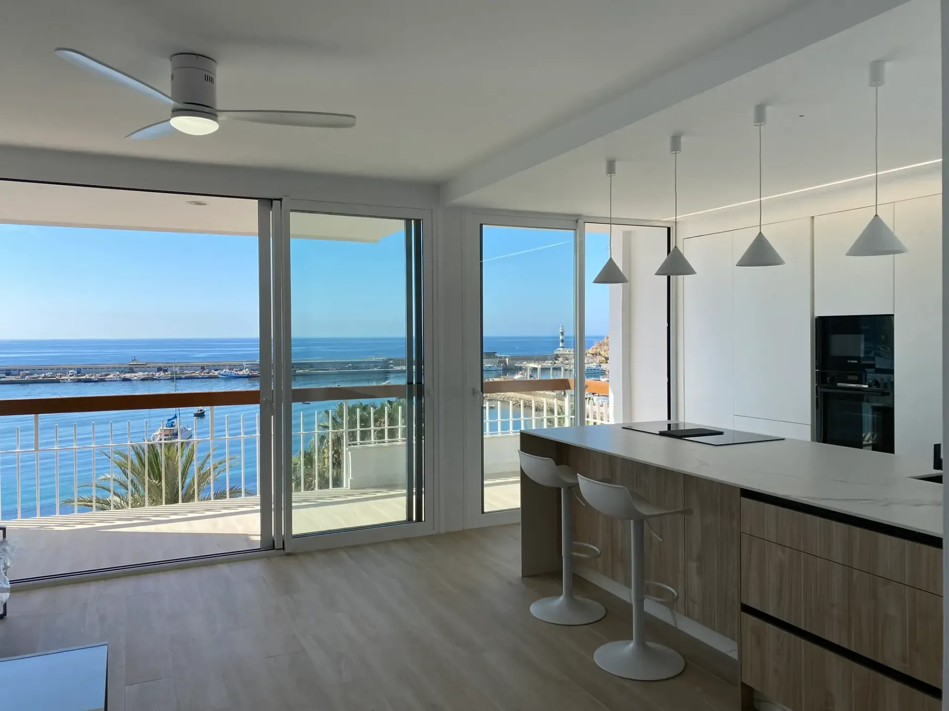Cocina moderna y luminosa con isla y taburetes, con acceso a un balcón y vistas al mar.