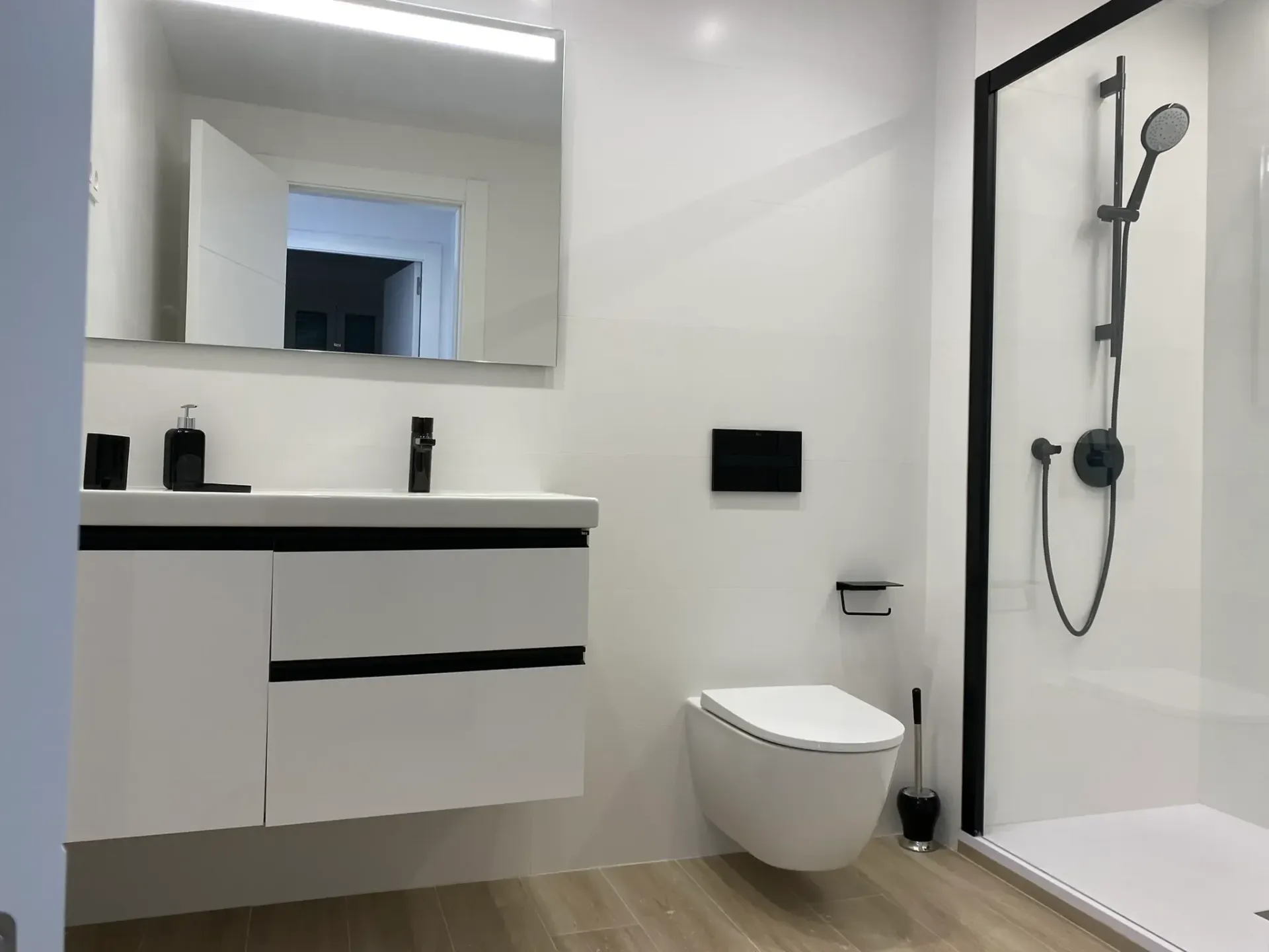 Baño moderno de color blanco con lavabo suspendido, espejo, inodoro suspendido y ducha de cristal.