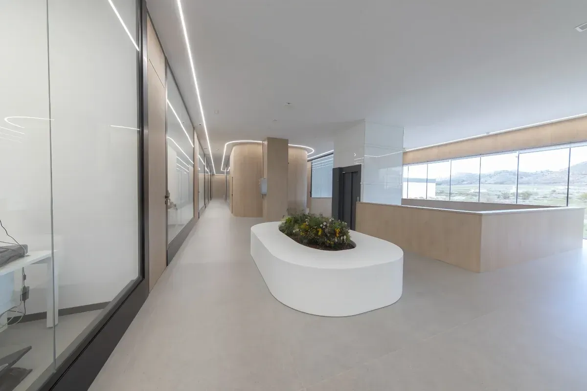Vestíbulo de oficina moderno y minimalista con paredes blancas, detalles en madera y un banco curvo con jardineras.