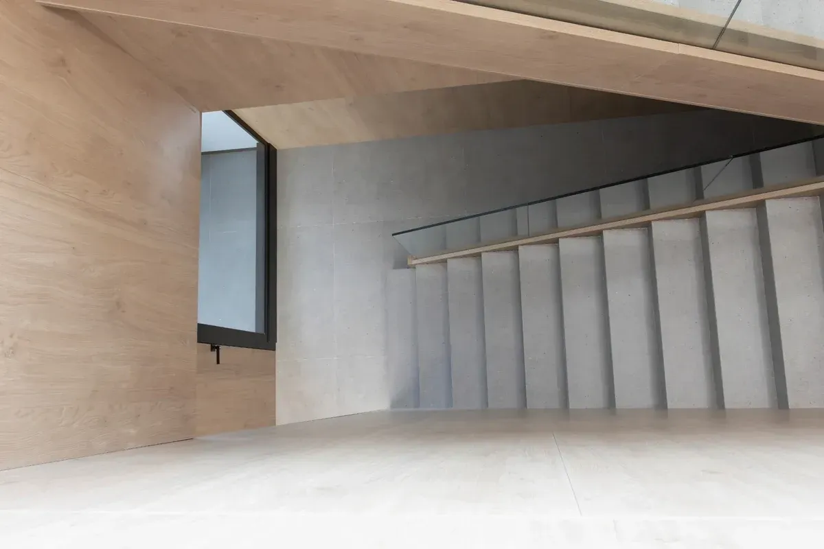 Escalera interior moderna con escalones grises, paredes de madera y pasamanos de metal.