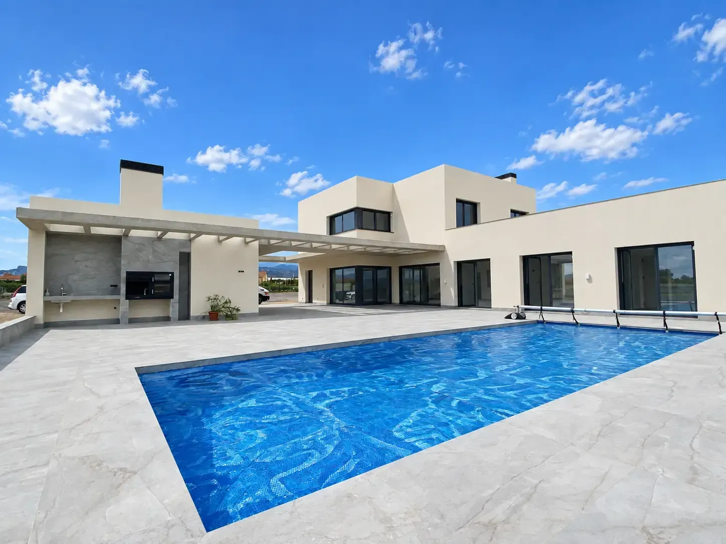 Casa blanca moderna con piscina azul y patio bajo un cielo brillante.