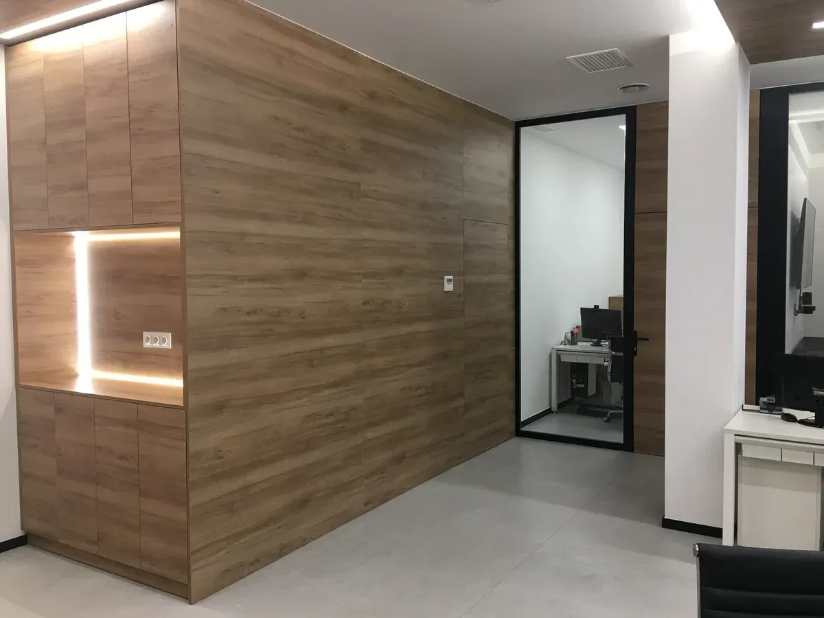 Pasillo de oficina moderno con paredes revestidas de madera, una puerta de cristal y suelo gris claro.