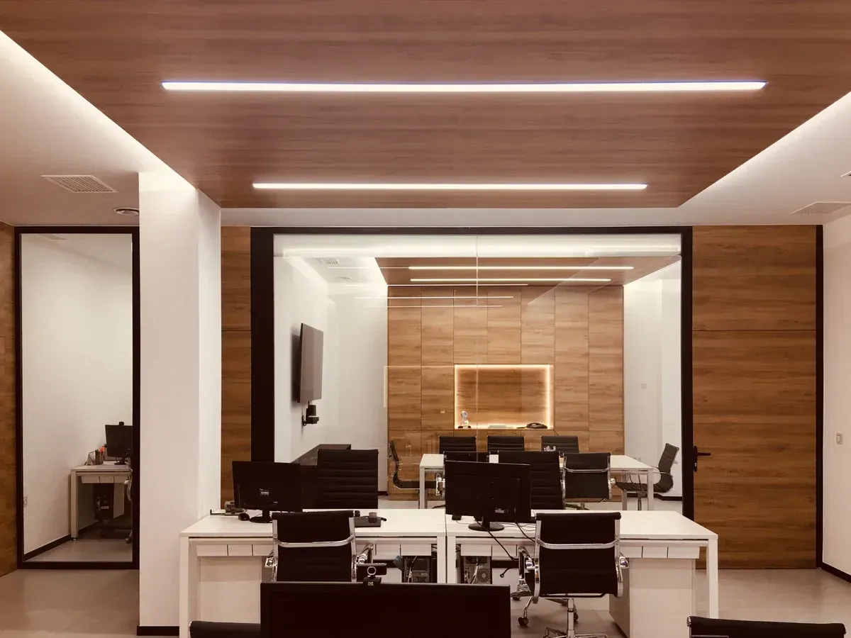 Moderna sala de conferencias con escritorios, sillas, revestimiento de madera e iluminación empotrada.