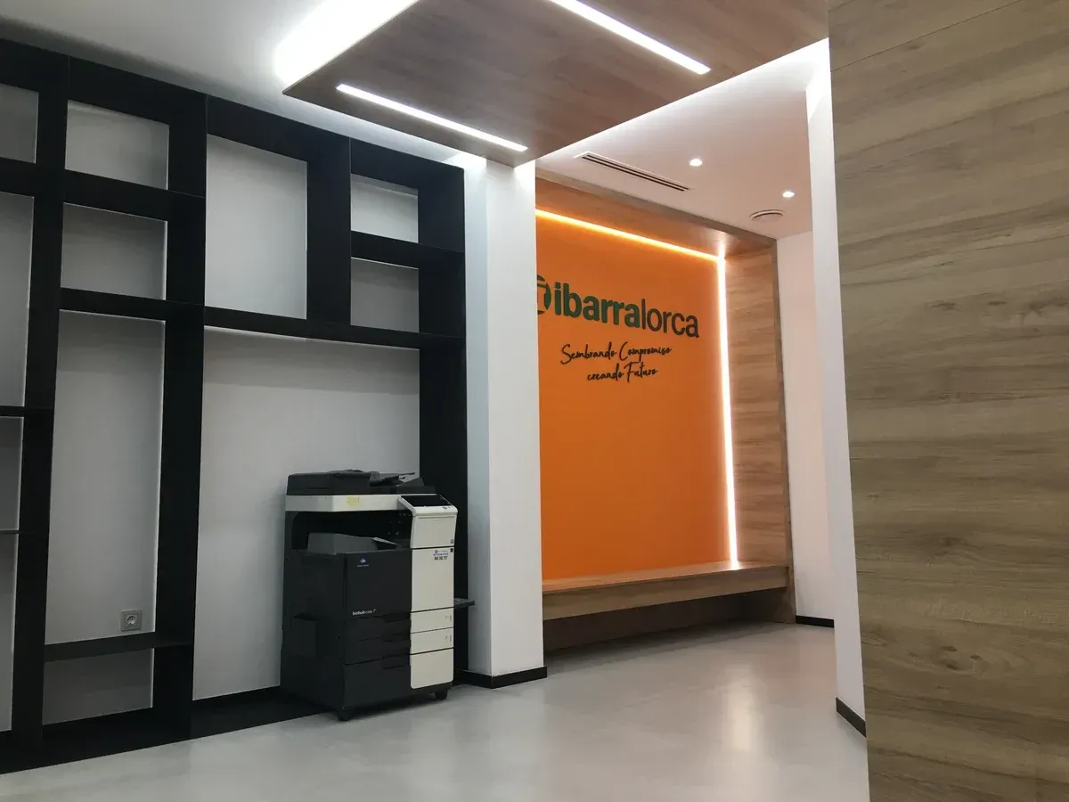 Vestíbulo de oficina moderno con estanterías negras, una impresora y una pared decorativa naranja con señalización.