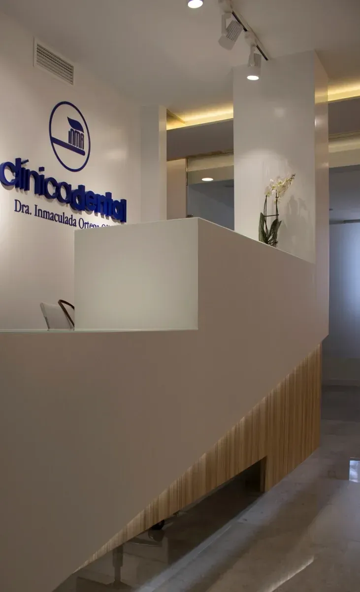 Mostrador de recepción de clínica moderna en un vestíbulo luminoso con paredes blancas y listones de madera.