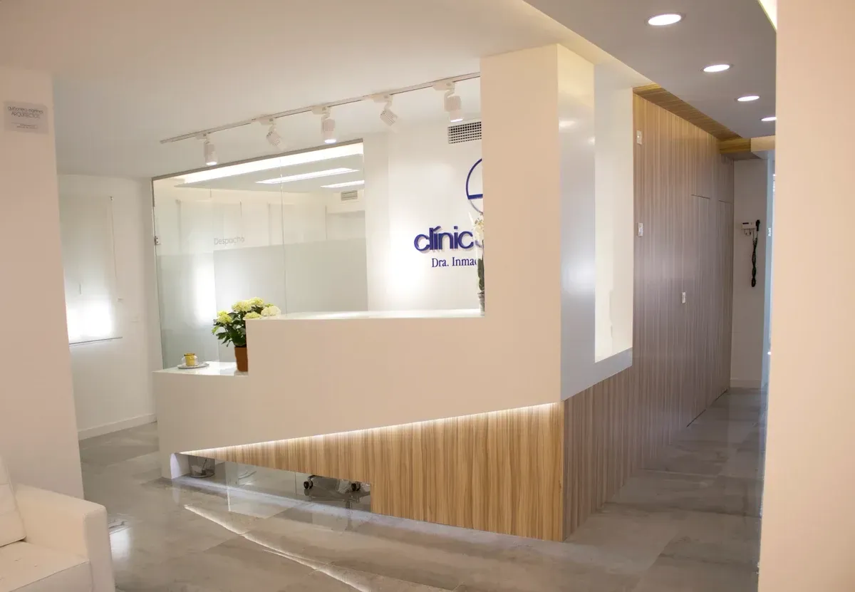 Luminosa y moderna zona de recepción de la clínica con paredes blancas, detalles en madera y mostrador de cristal.