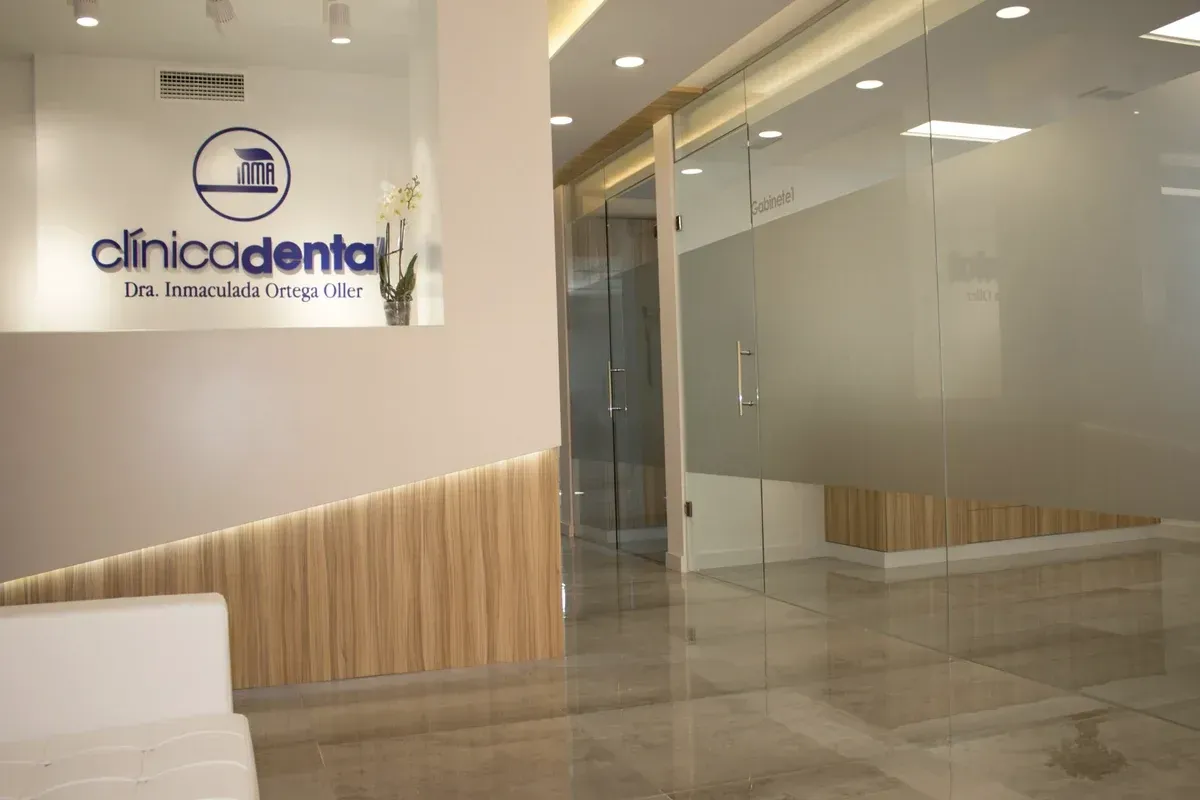 Área de recepción de la clínica dental con puertas de vidrio esmerilado y paredes blancas con detalles de madera.