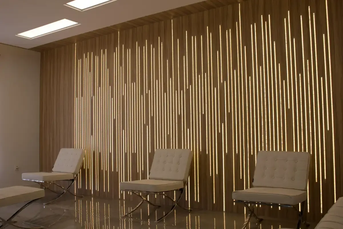 Sala de espera vacía con tres sillas de color beige y una pared decorativa revestida con listones de madera.