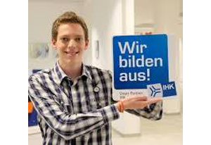 Ein Mann im karierten Hemd hält ein Schild mit der Aufschrift „Wir bilden aus“.