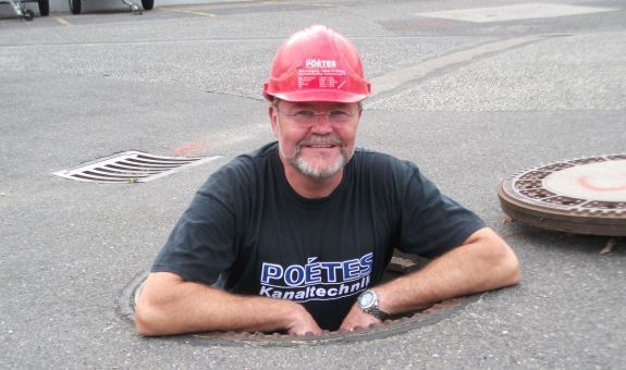 Mann schaut aus einem Gullideckel heraus - Rohrreinigung Mechernich - POETES Kanaltechnik 