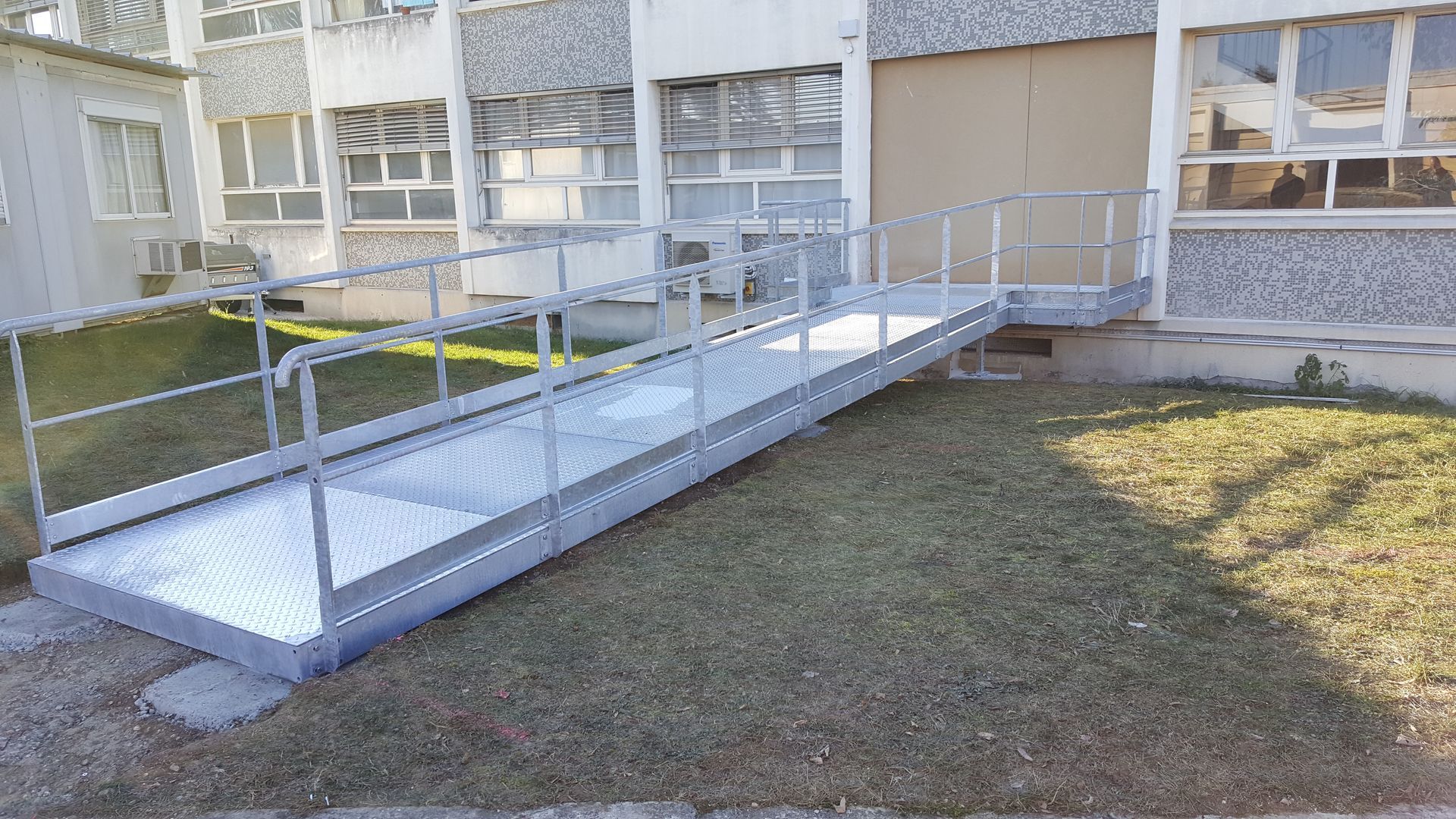 Une rampe d'accès métallique installée à l'extérieur, devant des bureaux.