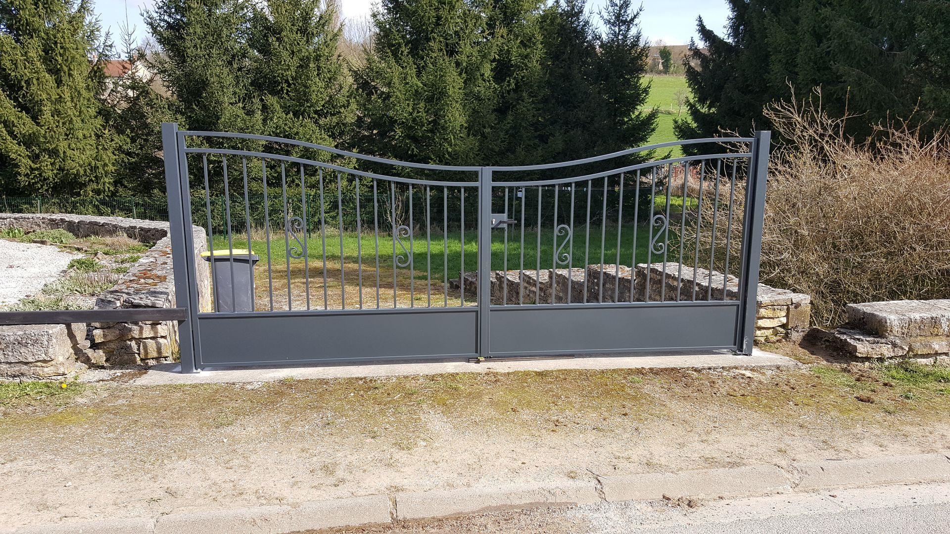 Portail métallique gris à l'entrée d'une allée de gravier.