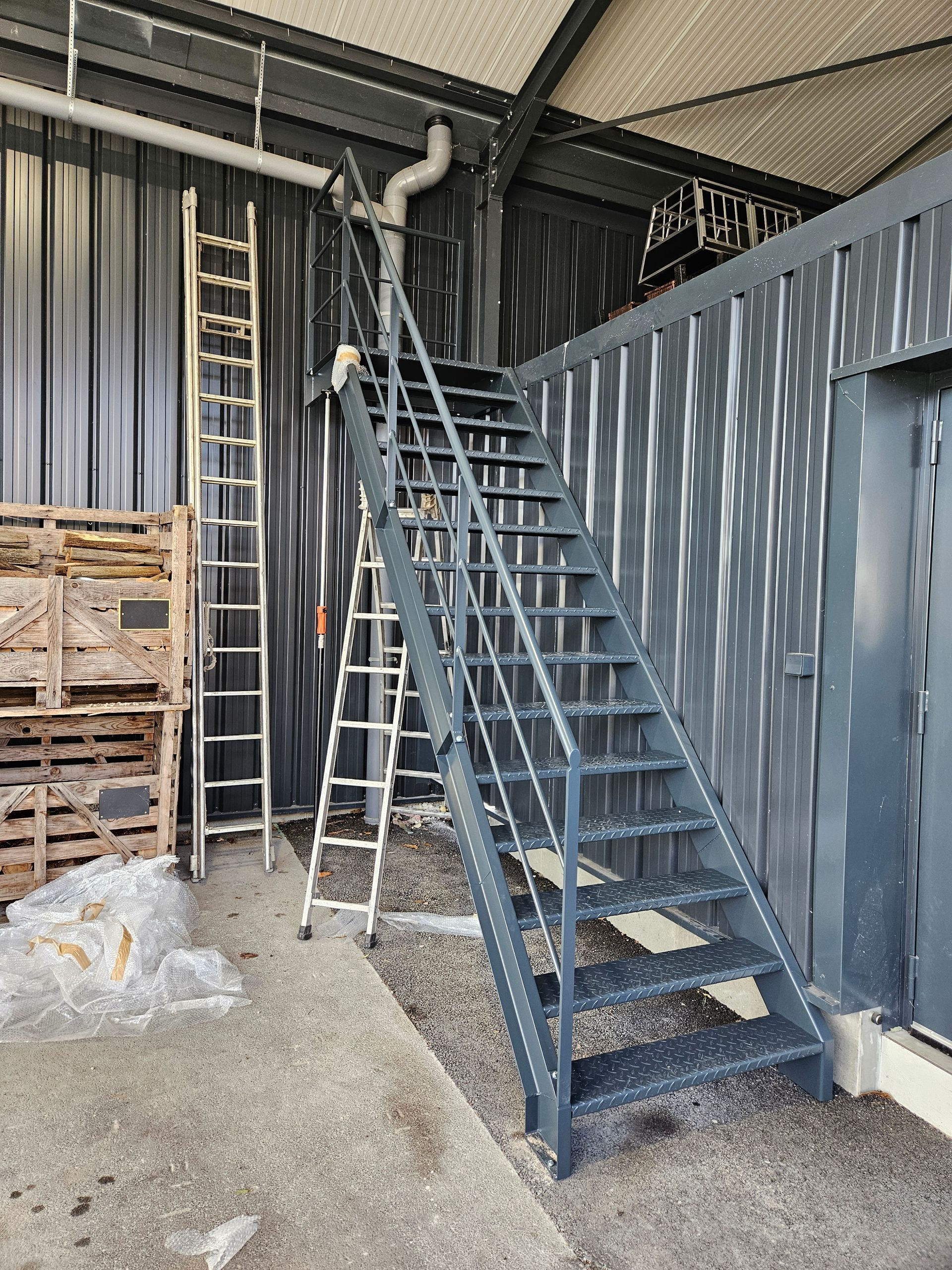 Escalier de service métallique avec plateforme et échelles dans un entrepôt.