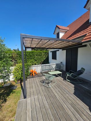 Pergola installée sur une terrasse en bois, dans un jardin ensoleillé.